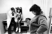 AIDS Ryan White sitting w/o shirt on examining table as his physician Dr. Martin Kleiman uses a stethoscope to listen to his lungs while mom Jeanne sadly looks on at hospital.  (Photo by Taro Yamasaki/The LIFE Images Collection/Getty Images)