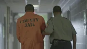 A prisoner being walked down hallway by guard