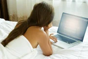 Beautiful woman is lying on the bed and using laptop pc