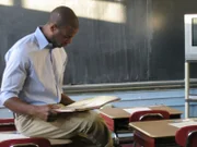 Actor, William Coleman (Keyon Pittman) sits on a desk reading a book.