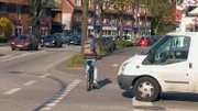 Ein Fahrradfahrer fährt knapp vor einem Transporter über Straße.