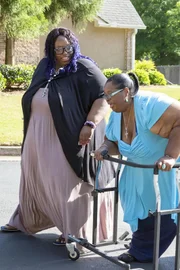 Shavonne walks by tired Chitoka using walker down street