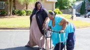 Shavonne walks by tired Chitoka using walker down street.