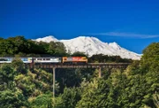 Zug fährt über das Viadukt neben einem schneebedecktem Berg    +++