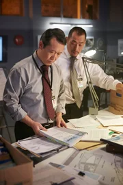 REENACTMENT - Lead Investigator (played by Oscar Hsu) looks through service bulletins while another investigator (played by a background preformer). (Photo Credit: Cineflex/Ian Watson)