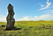 A tall stone menhir stands at the side of a field road that runs through the hilly steppe.