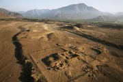 Luftaufnahme des Tempels und des Amphitheaters mit den noch nicht ausgegrabenen Pyramiden der heiligen Stadt Caral im Hintergrund.