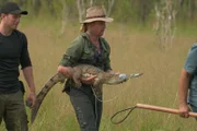 Damo hält ein Krokodil mit zugeklebtem Maul. Matt schaut zu.