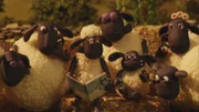 Shaun liest ein Buch über Drachen vor und die Schafe hören gespannt zu.