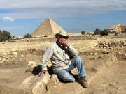 Dr. Mark Lehner sitzt neben einem großen Alabasterblock, der in dem neu entdeckten königlichen Gebäude in der Stadt der Pyramidenbauer gefunden wurde, mit der Großen Pyramide im Hintergrund auf dem Gizeh-Plateau in Kairo, Ägypten. (Windfall Films/Caterina Turroni)