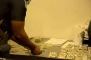 Stapel von Falschgeld liegen auf einem Inspektionstisch, während CBP-Beamter Ivey das Bargeld zählt, das im Gepäck eines Passagiers in Atlanta, Ga., in mehreren handgefertigten Bilderrahmen entdeckt wurde (National Geographic for Disney).
