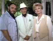 Jessica Fletcher (Angela Lansbury) ist zu Besuch bei ihrer Freundin Olivia auf Jamaika. Dort trifft sie auf Olivias Schwager Harry (John Rhys-Davies, li.) und dessen Nachbarn Jean-Pierre Dusant (Hurd Hatfield, mi.).