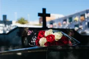 Weiße und rote Rosen auf schwarzem Granitgrabstein im Freien. Beerdigungszeremonie, im Hintergrund sieht man das schwarze Kreuz und den Rest der Grabsteine auf dem Friedhof