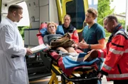 Ariane Bischof (Franziska Brandmeier, 2.v.l. mit Komparsin, h.) wird direkt vom Flughafen in das Johannes-Thal-Klinikum eingeliefert. Dr. Moreau (Mike Adler, l.) und Mikko Rantala  (Luan Gummich, 2.v.r. mit Komparse, r.) nehmen sie in der Notaufnahme auf.