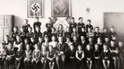 Ein Klassenporträt von jungen Schulkindern mit ihrem Lehrer vor einer Fotografie von Adolf Hitler und zwei Hakenkreuzen während des Zweiten Weltkriegs, um 1940.