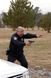 The officer holds a gun pointed at the suspect.