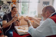 Mike (Harry Blank, links) und Hubert (Bernhard Ulrich, rechts) genießen gemeinsam eine Thunfischpizza.