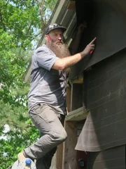 Matt steht auf einer Leiter und verkleidet eine Wand.