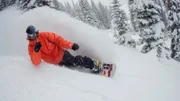 Mann rutscht auf einem Snowboard bergab.
