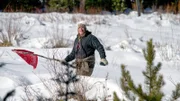 Cody Lundin stands in a snowy field using a red bandana on a stick to signal help.