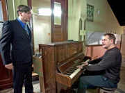 Stefan Merck (Martin Armknecht, li.) ist genervt von dem endlosen Klavier-Geklimper seines ungeliebten Mieters Georg Büttner (Stephan Schad, re.). Als Georg beim Auszug aus der Wohnung nichts Besseres zu tun hat, als wieder Klavier zu spielen, packt Stefan sofort mit an, um das Klavier endlich aus dem Haus zu schaffen.