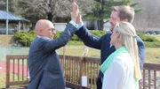 Host Anthony Melchiorri high-fives owner Shaun Lyons on the pool patio of Water Gap Country Club while Julie Lyons looks on, as seen on Travel Channel's Hotel Impossible.