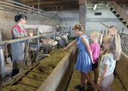 Luzia Kuppelwieser mit Kindern im Kuhstall und erklärt wo die Milch herkommt.