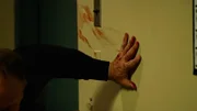Ein Mann klammert sich mit einer blutigen Hand an die Wand