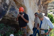 Eric Drummond, Chad Ollinger, and Charlie Snider prepare for Chad to enter the cave - Chad wears a hard hat, mask, and harness.