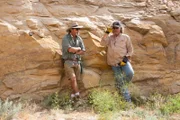 Eric Drummond and Duane Ollinger lean on a rock wall and talk.