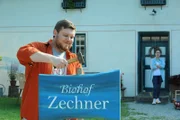 Severin (Andi Gießer) hämmert stolz das neue Bio-Hof Schild in den Boden.