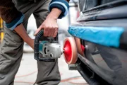 professional mechanic using a power buffer machine for cleaning the body of a car from scratches. Detail of car care concept