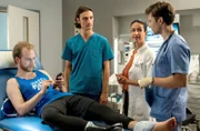 Während der Patient Bastian Kempe mit seinem Handy beschäftigt ist, besprechen Dr. Leyla Sherbaz, Florian Osterwald und Ivo Maric den weiteren Behandlungsverlauf.