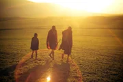 Maasai-Stammesangehörige wandern bei Sonnenuntergang durch die Serengeti.