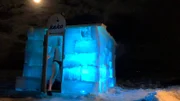 Ein Mann verlässt im Dunkeln die von innen beleuchtete Eis-Sauna in Lappland.
