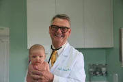Dr Robert holds a baby.