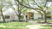 The exterior of the Morgan remodeled home has white painted brick, a fresh landscape, large wooden windows, and rock-framed flower beds, as seen on Fixer Upper.