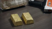 Goldbarren werden auf einen Inspektionstisch gelegt, während HSI-Agenten in der Nähe eine Nachbesprechung über einen untersuchten illegalen Goldabbau in Miami durchführen.