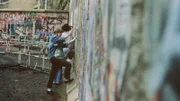 SRF school DDR in 10 Minuten – Mauerbauer und Mauerspechte Folge 8 Junge Menschen stehen vor der Berliner Mauer.