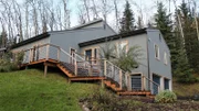 Exterior of house from driveway, shot of stairs leading to the front door, grey wood paneling with blue garage doors, on one of the stops in the Hunt family house search, Chena Forrest Drive, Fairbanks, Alaska.