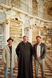 Moderations-Duo "2:tagesbart" (Pascal Kitzmüller, l.; Karl Weixelbaumer, r.) posiert für ein Foto mit Pater Egon (m.)