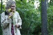 A woman happily walks through the woods with flowers.