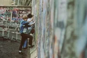 Junge Menschen stehen vor der Berliner Mauer.