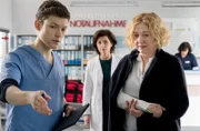 Da die Stimmung zwischen Karin Patzelt (Marijam Agischewa, M. mit Komparsin, h.) und ihrer ehemaligen Kommilitonin Gitta Baselow (Charlotte Crome, r.) leicht angespannt ist, wird Florian Osterwald (Lion Wasczyk, l.) die Patientin zugeteilt.
