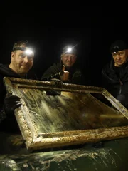 L-R: Josh Gates und die Ermittler Pawel Piatkiewicz und Robert Kubiszekski entdecken in dem Nazitunnel einen verfallenen Bilderrahmen aus Holz und Glas.