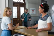 Während Hausmeister Winkler (Steffen Wolf, M.) die Eingangstür ausmisst, sprechen Christin Lange (Sarah Thonig, l.) und Miriam Stockl (Marisa Burger, r.) über die bevorstehende Lieferung der Aktenschränke.