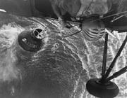 A U.S. Marine Corps helicopter attempts an unsuccessful recovery of the Mercury-Redstone 4 "Liberty Bell 7" spacecraft. The spacecraft hatch opened prematurely, and astronaut Virgil I. Grissom, pilot, escaped into the water. The helicopter hooked onto the spacecraft but could not retrieve it. Grissom was recovered by another helicopter and flown to the recovery ship, USS Randolph. The Mercury spacecraft sank to the bottom of the ocean.