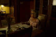 Reconstructions of an actor playing Virginia sitting at the kitchen table writing in a notebook.