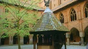 Ein Innenhof der Burganlage von Burg Malbork mit gotischen Stilelementen an Fassade und Brunnen.