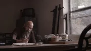 Bearded man sits with smoke in the air.